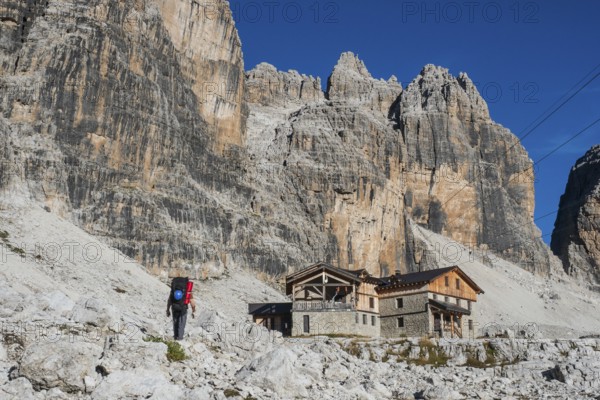 Tourist with hiking backpacks in mountain hike on summer day. Man traveler hiking in beautiful mountain landscape. Climber and alpine hut Angelo Alimonta in Dolomites Alps, Italy