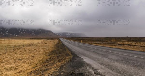 Rural Ring empty highway in Iceland with mountains covered with mist and fields in yellow color