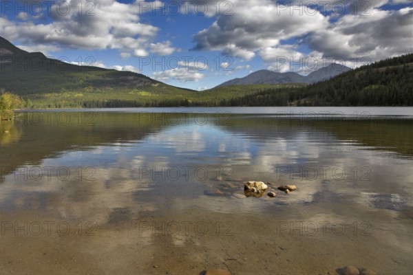 Clouds shining on the sun are reflected in northern lake surrounded by mountains