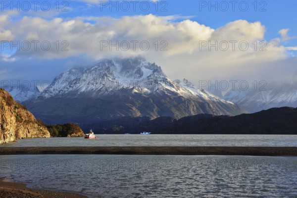 Gray lake and snow-capped mountains. By the banks of the red tourist ship sails. Summer sunset illuminates the lake. National Park Torres del Paine, Chile
