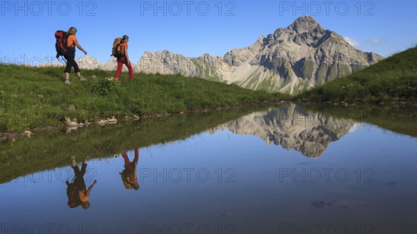 Two female mountaineers are reflected in a lake by the majestic Biberkopf in the background, Allgäu Alps, Oberstdorf, Bavaria, Germany
