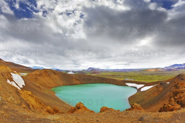 Summer in Iceland. Picturesque lake in the crater of an extinct volcano. Lake water bright green color. On the shores lie snowfields from last year