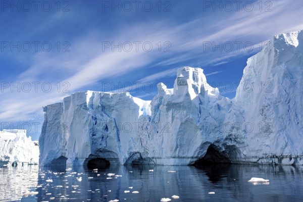 Ice formations with caves and reflections in the water under a blue sky, icebergs in the Southern Ocean in Antarctica