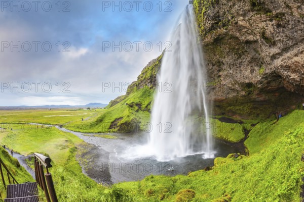 Seljalandsfoss waterfall in July. Large rainbow decorates a drop of water. The warm July day in Iceland