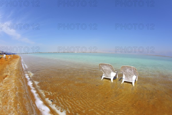 Two white beach armchairs stood side by side in the water at the beach. Dead Sea, Israel