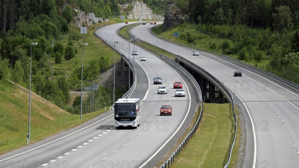 Summer motorway landscape with white Iveco Evadys tour bus among car traffic. Salo, Finland, June 30, 2018