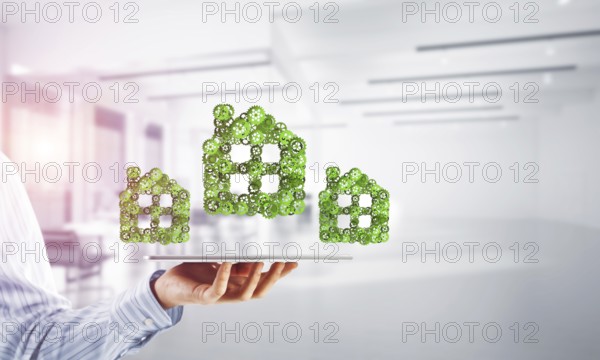Close of businessman holding tablet pc with house sign made of connected gears. Mixed media