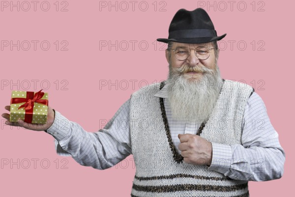Portrait of aged man with gift box. Isolated on pink