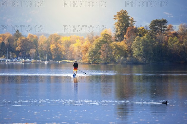 An image of a stand up paddling man at autumn the lake