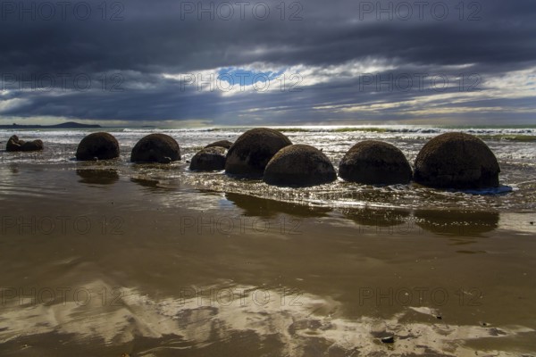 Moeraki boulders - group of large round boulders. The coast of New Zealand. The sun's rays are reflected in the ocean water. The Pacific ocean tide begins. The concept of ecological, exotic and phototourism