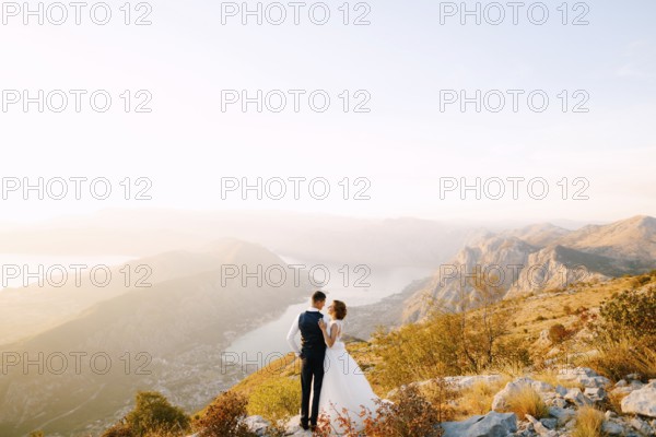 The bride and groom stand on the top of Mount Lovcen overlooking the Bay of Kotor, smile and hug tenderly .