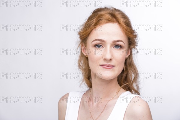 Portrait of a beautiful young woman of European, Caucasian nationality with long red hair and freckles on her face posing on a white background in the studio. Close-up student girl in a white blouse