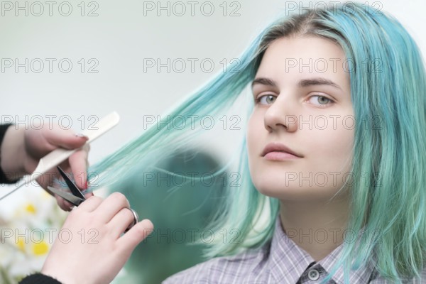 Hairdresser cutting with scissors long green hair of young woman. Hair care in professional beauty salon