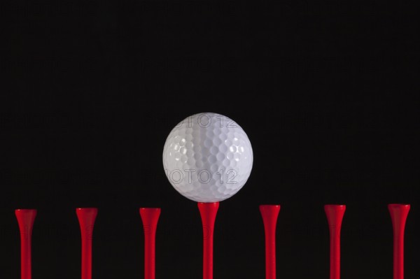 Golf ball and red tee on a black background