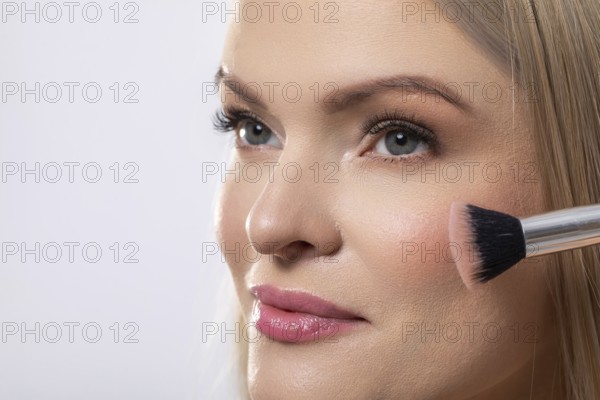 This is a professional makeup application showcasing a model skillfully utilizing a blush brush for enhancement