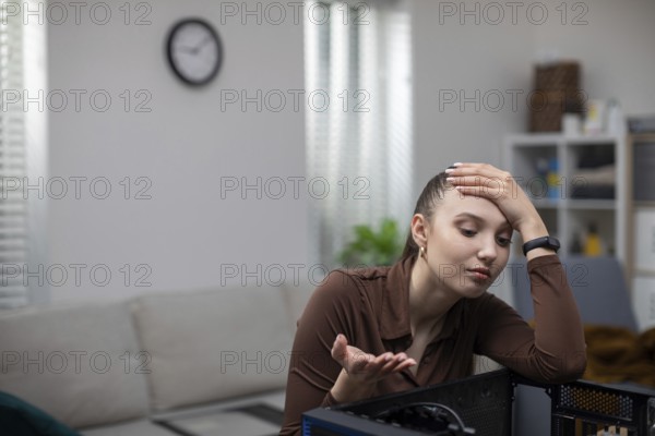 A young woman catches her head in a gesture of helplessness while fixing her computer. A girl sits at a table and tries to fix a computer. Blurred background. In the background you can see a white wall and a clock hanging on it