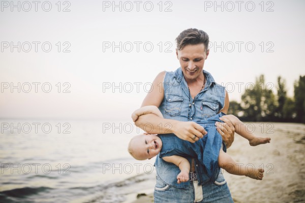 Theme Fatherhood and rest with a child at sea. Young handsome Caucasian father plays plays enjoys throwing up in arms his child up in summer daughter on the sandy beach on the seashore