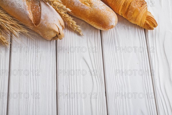 Baguettes and croissant wheat ears on wooden boards with copyspace