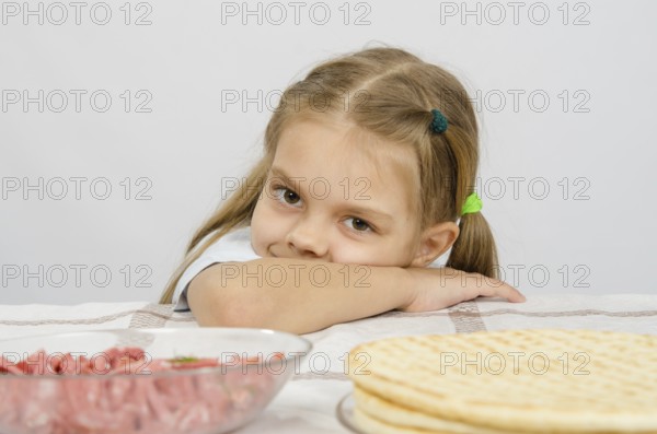 Little girl sitting at a table with his head on his hand with a smile and looking at the food in front of her