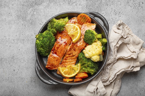 Healthy baked fish salmon steaks, broccoli, cauliflower, carrot in black cast iron casserole bowl on grey rustic stone background. Cooking a delicious low carb dinner, healthy nutrition concept, food photography, food photography