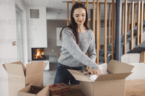 Young caucasian woman wrapping a gift, getting it ready to send in the post. Woman packaging a surprise gift for a family member, packaging it into a brown cardboard box