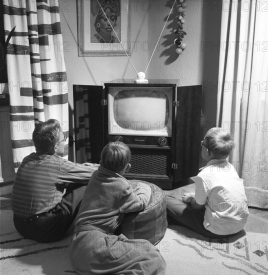 Television set in the 1950s. An early television set in period design wooden cabinett with only the ability to display television broadcasts in black and white. The antenna is seen standing on the tv. The knobs on the front control the picture and sound. The three boys in front of it looks at it in fascination. 1956 Svahn ref SVA1