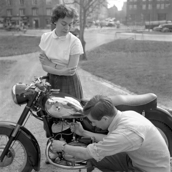In the 1950s. A man on his Puch motorcycle with a woman looking at him while he checks the fuel valve. Sweden 1955