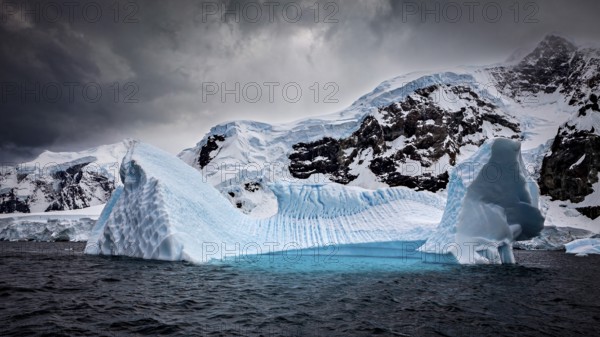 A huge iceberg under a threatening cloudy sky in an icy environment, icebergs in the Southern Ocean in Antarctica