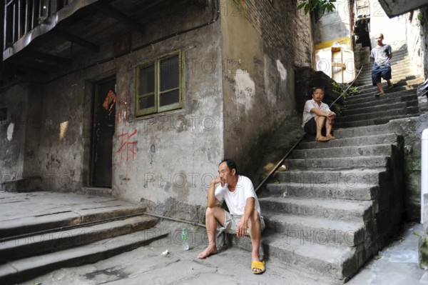 04.08.2012, Chongqing, China, Asia, Men sit on the steps in front of a house in the old town of Chongqing, on the wall of which characters painted in red inform the residents that the old house will soon be demolished to make way for new buildings. The megacity lies at the confluence of two main waterways, the Yangtze and Jialing rivers, and is one of the fastest growing metropolises in the world
