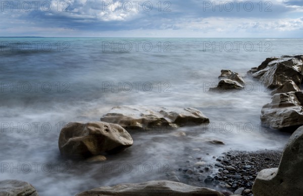 Seawaves splashing onto the sandy coast with pebbles and blue cloudy sky. Melanda coast, Pissouri Cyprus. Long exposure photography