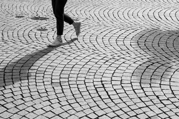 Feet and legs of a person walking on cobbled street