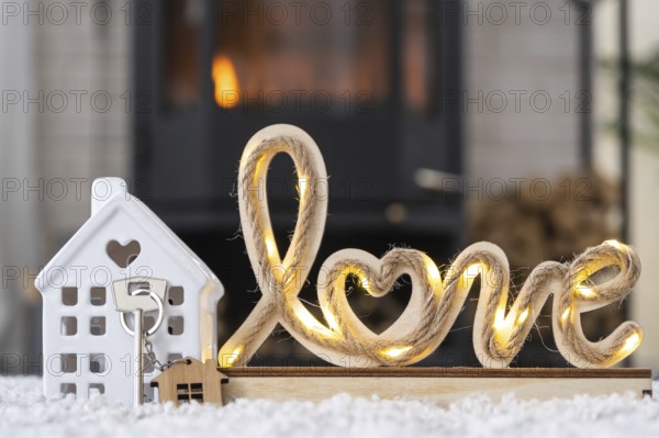 Key to house with keychain against background of fireplace stove with fire and firewood in Valentine decor, love home. Moving to new house, mortgage, rent and purchase real estate