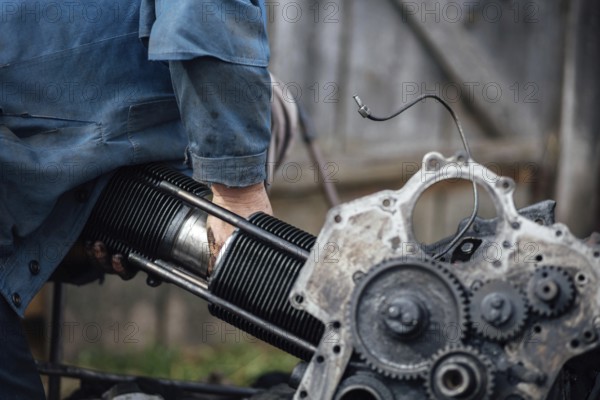 A person working on an engine outdoors, focusing on metal and mechanical components