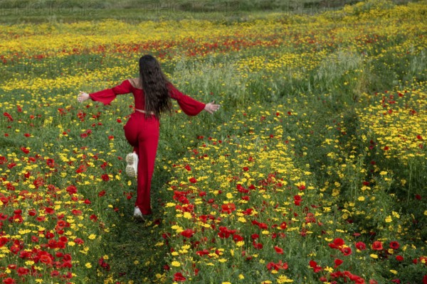 Happy woman wearing red dress running in the field in spring. Spring time blooming flowers