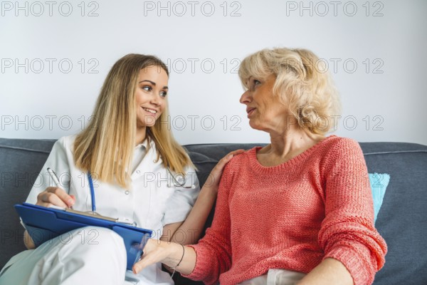 Young blonde woman caregiver helping senior woman at home. Nurse assisting her old woman patient at nursing home. Senior woman being helped by nurse at home.
