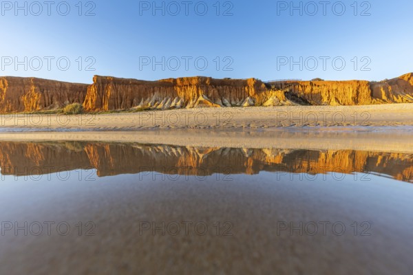 A landscape on the beach at low tide. The surrounding rocks and cliffs are reflected in the sea at sunset. Praia da Falésia, Algarve, Portugal
