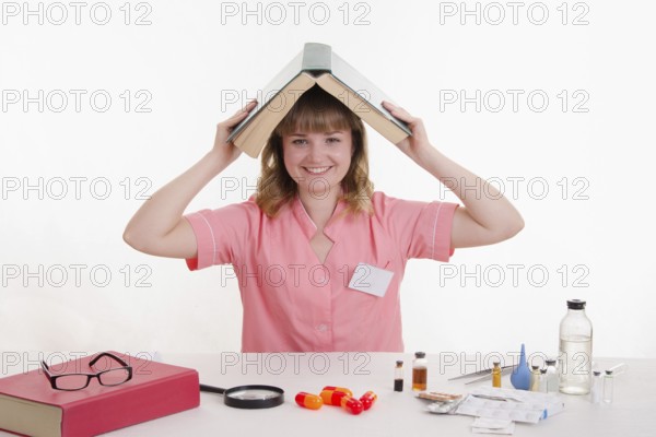 Pharmacist sitting at the table reading a thick handbook of medicines