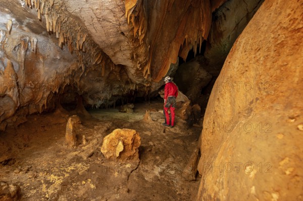 A speleologist with helmet and headlamp exploring a cave with rich stalactite and stalagmite formations. graphy