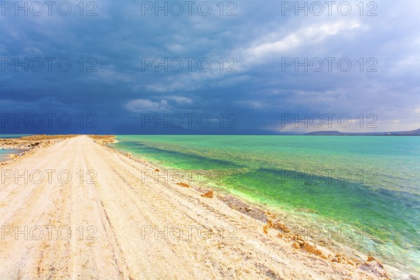 Low winter clouds are reflected in the green sea water. The landfill embankment runs through the sea. Winter thunderstorm begins. Israel. The picturesque Dead Sea