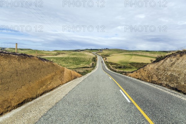 South Island, New Zealand. Incredible cloudy sunset. Great asphalt highway among green fields and hills. Lush cumulus clouds are lit by the sun. Southern Scenic Route. The concept of active and photo tourism
