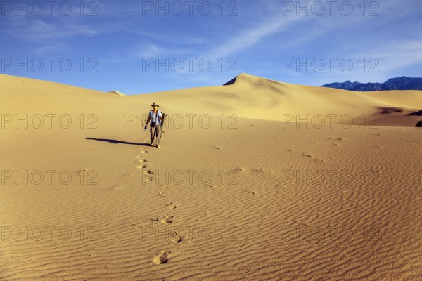 Woman with a camera and a tripod goes among the dunes. USA. Mesquite Flat Sand Dunes, Death Valley, California. Light sand waves from the desert wind. Concept of active and photo tourism