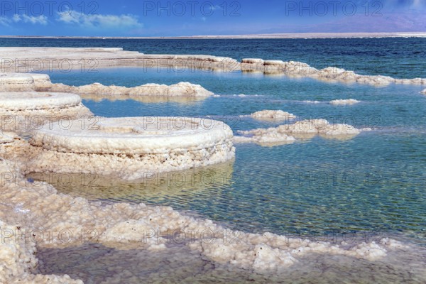 The evaporated salt forms bizarre crystal shapes on the surface of the water. Israeli coast, warm winter February day. Unique Dead Sea. The drainless salt lake in the Middle East
