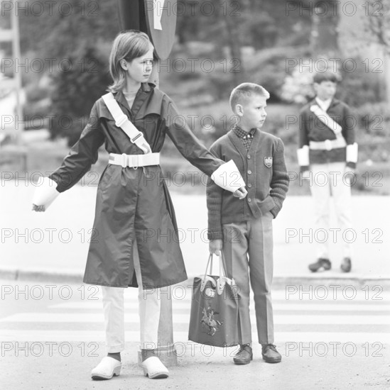 Junior safety patrol in the 1960s. A teenage girl stands with her arms out and signals to the pedestrians to stop at the crosswalk. When the cars have passed or stopped, the children can walk across the street. Being part of the Junior safety patrol was voluntary for the school students and the reward was sometimes to go on shorter trips and excursions. Nowadays, the operation is closed in many municipalities. Sweden 1964
