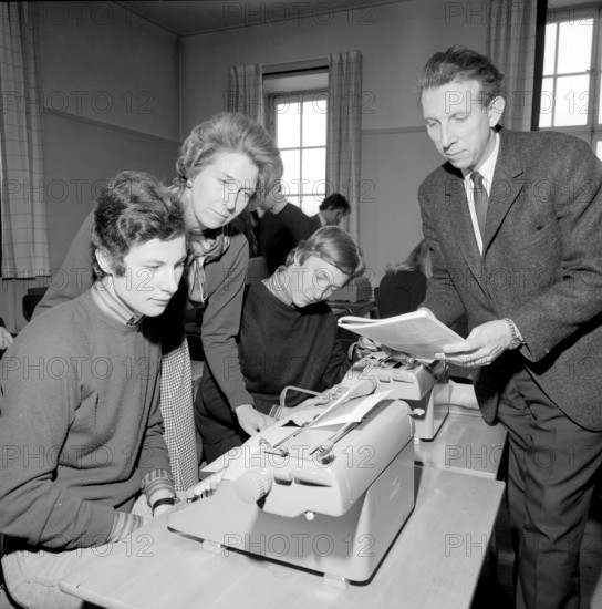 Learning to type in the 1960s. A classroom of students sitting at typewriters. A class and education in typing, using the right fingers and keys. Two teachers in the picture. 1968. Conard ref 5573