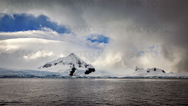 White mountains and clouds are reflected in the dark waters of Antarctica, The coast and landscape of Antarctica