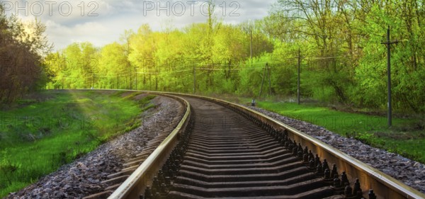 Morning landscape on the railway tracks. The sun's rays are the green grass and the rails on which the train travels. Trees along the railway