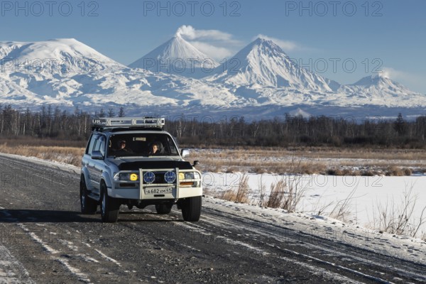 Japanese Sport Utility Vehicle Toyota Land Cruiser driving along road on background beautiful winter landscape, active Kluchevskoy Volcano on sunny day. Kamchatka Peninsula, Russia, January 7, 2016