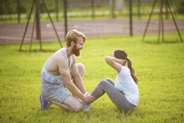 Sit ups fitness couple exercising sit up outside in graß Fit people working out cross training. Woman doing abdominal crunches press exercise with trainer. Couple Doing Sit-Ups Abdominal Crunch