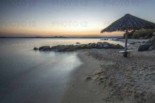 View through rocks on a sandy beach into the sunset. Landscape shot with view to the horizon over the wide sea at the coast of Ouranoupoli, Thessaloniki, Central Macedonia, Greece