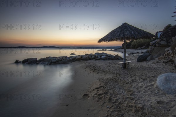 View through rocks on a sandy beach into the sunset. Landscape shot with view to the horizon over the wide sea at the coast of Ouranoupoli, Thessaloniki, Central Macedonia, Greece